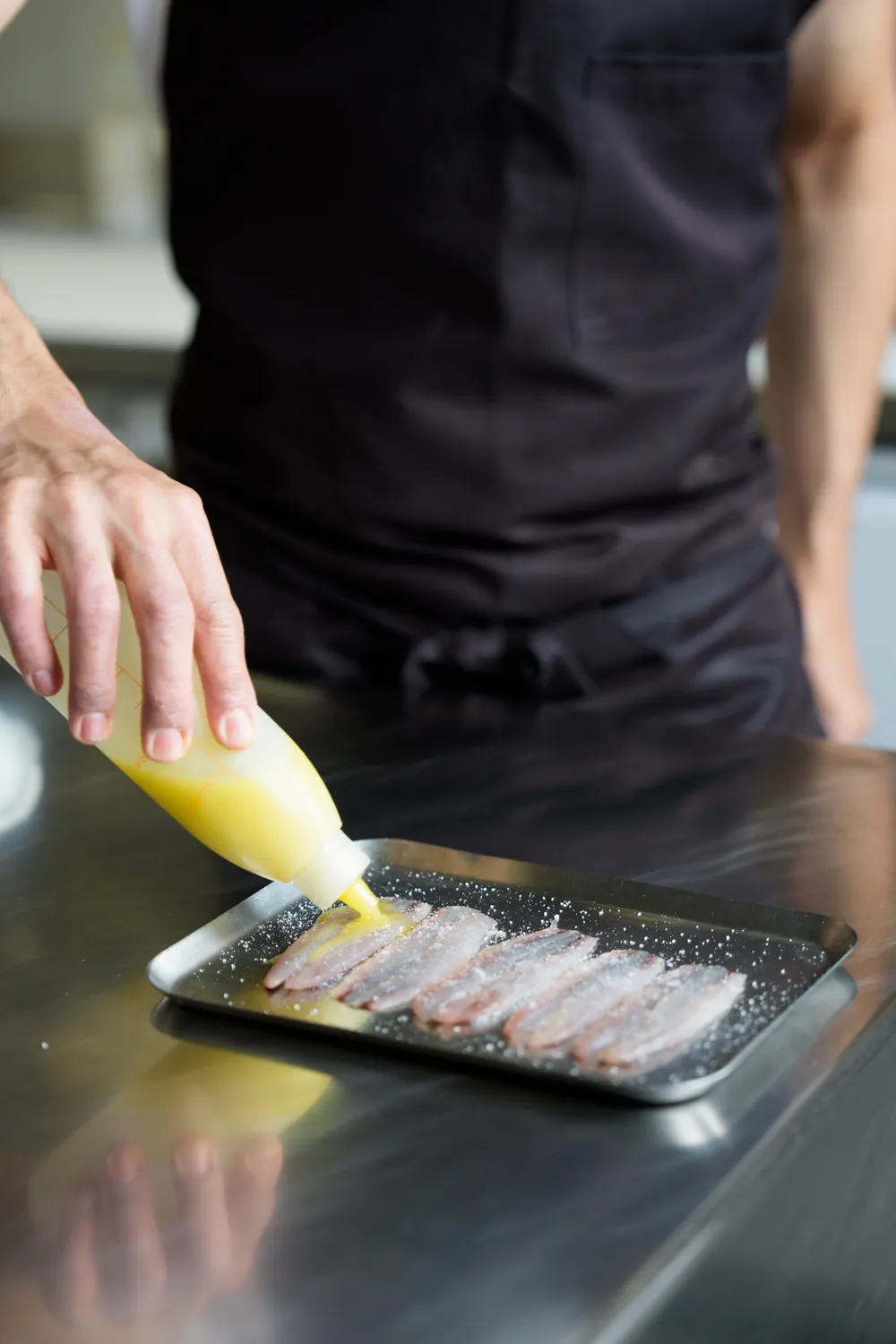 Il cuoco condisce i filetti di pesce azzurro allineati sulla teglia